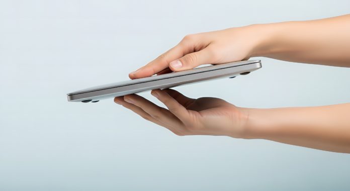 Hands holding ultra thin silver laptop on light blue background